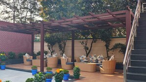 A covered outdoor seating area with wooden furniture and potted plants. - Empires Hotel Paradip (Kujang)