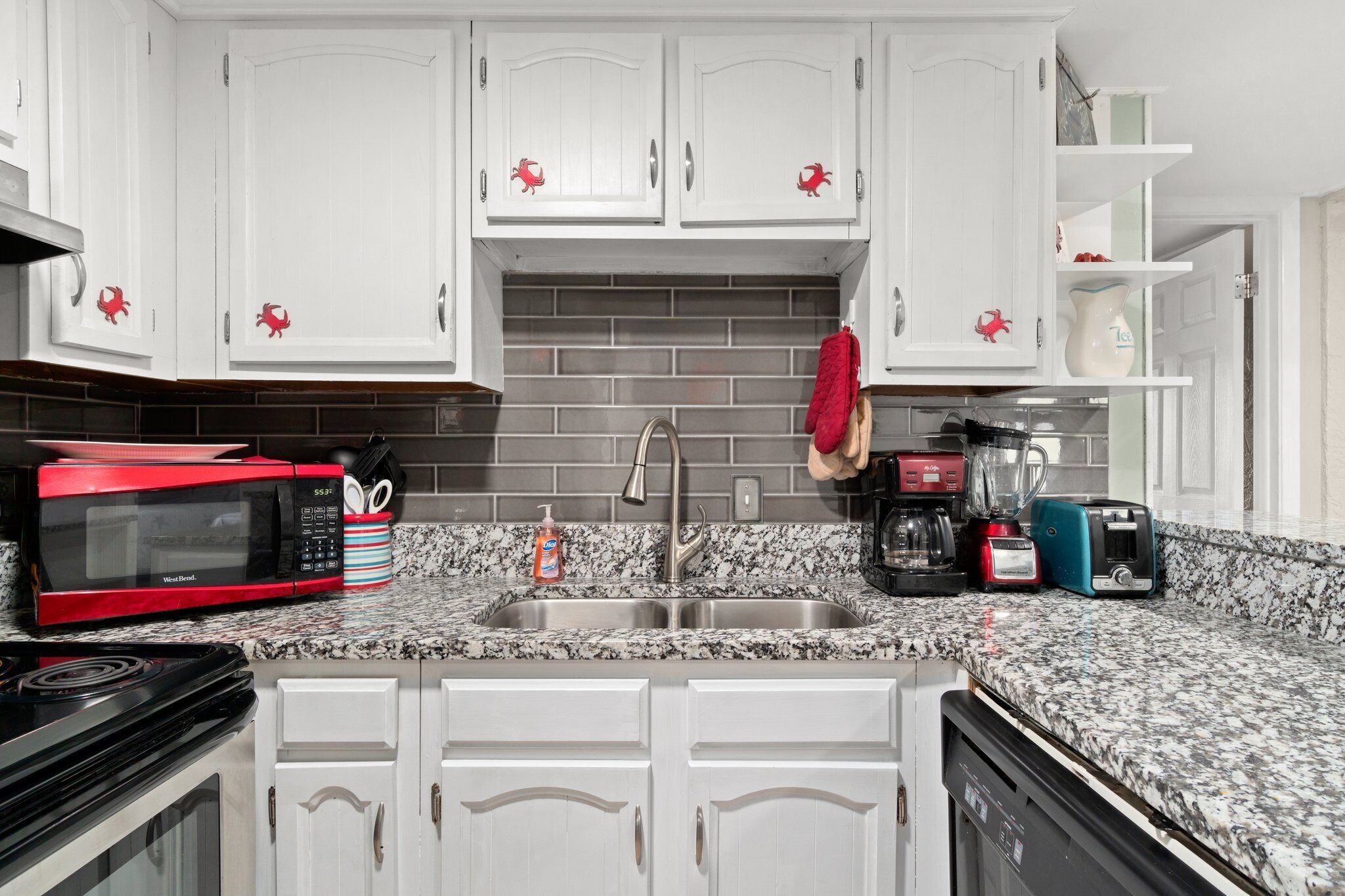 A kitchen with white cabinets, a granite countertop, a red microwave, a sink, and a coffee maker.