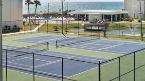 A tennis court with a pool and beach view, surrounded by palm trees and a building. - Sept 15-19 Reduced! Steps to the Beach & Tootsies! (Panama City Beach)