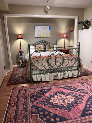 Een slaapkamer met een bed, twee bedlampen, een decoratief wandkunstwerk en twee vloerkleden.
