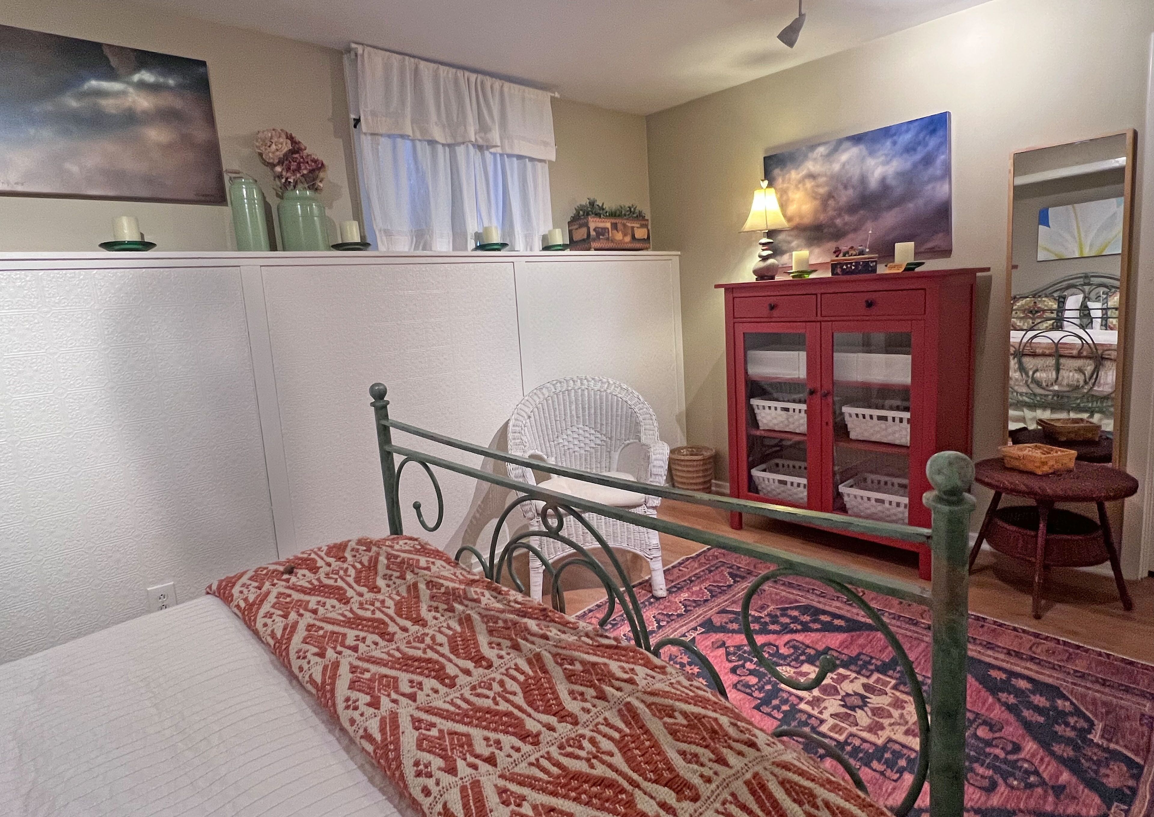 Un dormitorio con una cama, una silla, un armario con cestas y un cuadro en la pared.