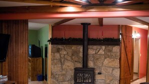 A cozy living room with a stone fireplace, wooden beams, and a television on a wooden stand. - Private Lodge Near Trails & River • Sauna • Sleeps 8 (Decorah)