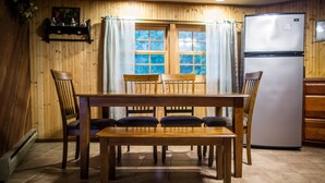 A wooden-paneled room with a dining table and chairs, a refrigerator, and a window with curtains. - Private Lodge Near Trails & River • Sauna • Sleeps 8 (Decorah)