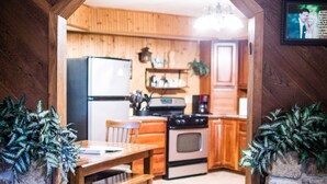 A cozy kitchen with wooden cabinets, a stone wall, and a dining area with a table and chairs. - Private Lodge Near Trails & River • Sauna • Sleeps 8 (Decorah)