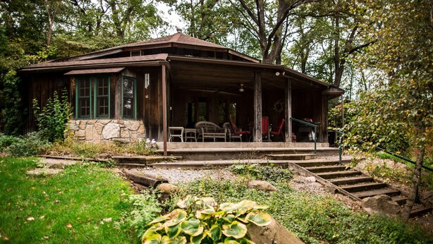 A rustic cabin with a stone foundation, a porch with outdoor seating, and a staircase leading to the entrance. - Private Lodge Near Trails & River • Sauna • Sleeps 8 (Decorah)