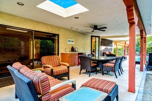 Un patio techado al aire libre con mobiliario de mimbre, una mesa de comedor y un ventilador de techo.