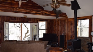 A rustic cabin interior with a wooden ceiling, a ceiling fan, a fireplace, a television, and a couch. - Allure charming peaceful wooded Hill Country like views with easy Lake access (eastland)