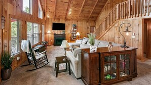 A wooden interior with a fireplace, a sofa, a rocking chair, and a staircase. - Lakeside Lodge – Private Dock, Hot Tub, Fire Pit & 8 Kayaks (Speedwell)