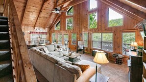 A spacious living area with a high ceiling, large windows, and a cozy seating arrangement. - Lakeside Lodge – Private Dock, Hot Tub, Fire Pit & 8 Kayaks (Speedwell)