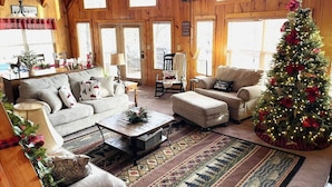 A cozy living room with a large Christmas tree, wooden walls, and a fireplace. - Lakeside Lodge – Private Dock, Hot Tub, Fire Pit & 8 Kayaks (Speedwell)