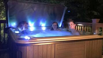Ein Whirlpool mit drei Personen darin, umgeben von einer Holzterrasse und Bäumen.