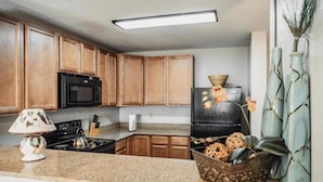 A kitchen with wooden cabinets, a black refrigerator, a stove, and a countertop with a decorative lamp and a basket of wicker balls. - Sweet Berry Patch-Unit 3706 - FREE Attraction Ticket with EACH night Stay Including Dollywood (Pigeon Forge)