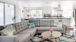 A modern living room with a grey sectional sofa, a round coffee table, and a view of the kitchen area. - Private Oasis over half an acre with private Pool & Spa. City ID 4059 (Palm Springs)