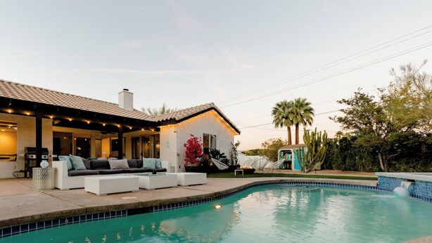 A swimming pool with a tiled edge, a covered patio area with outdoor furniture, and a small building with a tiled roof. - Private Oasis over half an acre with private Pool & Spa. City ID 4059 (Palm Springs)