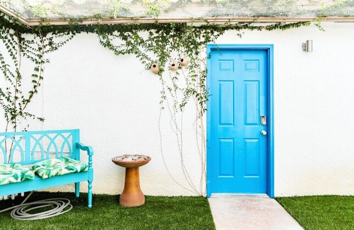 A blue door, a blue bench, and a small table with a plant.