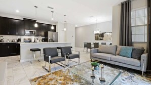 A modern living room with a sofa, two armchairs, a coffee table, and a glass-top dining table. There is a kitchen area with dark cabinets and a microwave. - Resort Townhome 4Bd Pool and Water Park 4841 (kissimmee)