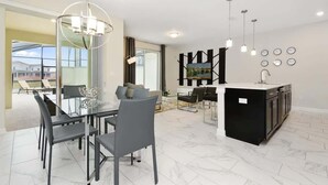 A modern kitchen with a central island, a dining area with a glass table, and a living space with a TV and wall clocks. - Resort Townhome 4Bd Pool and Water Park 4841 (kissimmee)