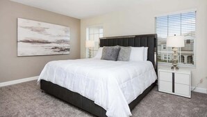 A bedroom with a large bed, a nightstand, a lamp, and a window with blinds. - Resort Townhome 4Bd Pool and Water Park 4841 (kissimmee)