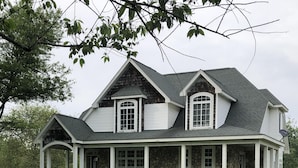 Een groot, twee verdiepingen tellend huis met een veranda rondom, een stenen fundering en een steil dak.