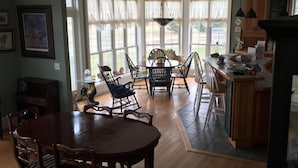 Een ruime eetruimte met een houten tafel en stoelen, een keuken met kasten en een aanrecht, en grote ramen voor natuurlijk licht.