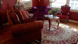 Ein Zimmer mit rotem Teppich, einem violetten Sofa, einem Holztisch und einem roten Sessel.
