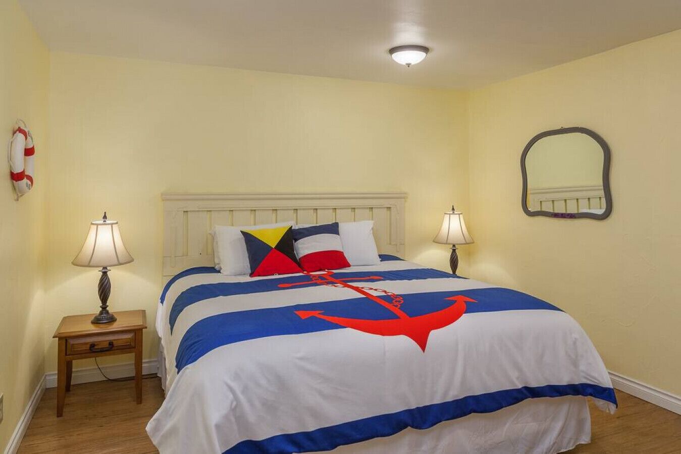 A hotel room with a bed, two bedside tables, a lamp on each table, a wall-mounted mirror, and a life preserver decoration on the wall.