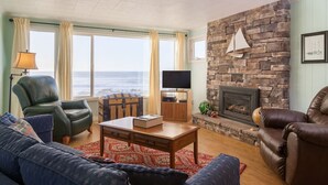 Una sala de estar con chimenea de piedra, sillones de cuero, televisor y vista al océano.