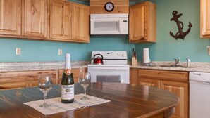 Una cocina con armarios de madera, un microondas blanco, un reloj, una estufa y una mesa con una botella de vino y dos copas.