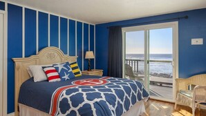 Un dormitorio con cama, mesita de noche, lámpara y vista al océano.
