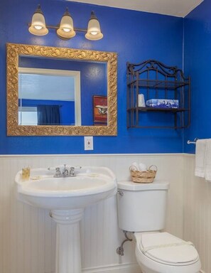 Une salle de bain avec un lavabo blanc, des toilettes et un miroir doté d’un cadre doré.