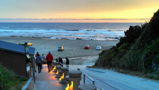 Una carretera costera que lleva a una playa con coches estacionados en la arena.