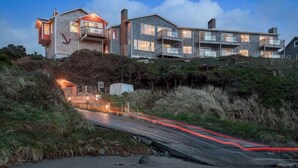 A coastal property with a road leading to a gated entrance, featuring a stone facade and multiple balconies.