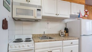 A kitchen with white cabinets, a stove, a microwave, a sink, and a refrigerator.