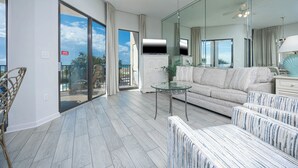 Un amplio salón con un sofá grande, una mesa de centro de vidrio y un balcón con vista al océano.
