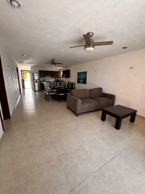 A spacious living area with a sofa, a coffee table, and a dining table set for four. A ceiling fan is visible, and the room has a neutral color palette. - In front of the beach with power and wifi included! (CHUBURNÁ PUERTO)