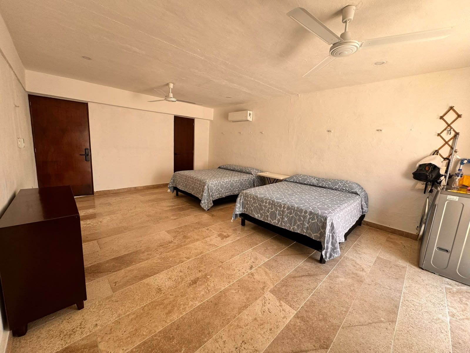 A room with two beds, a ceiling fan, a wooden door, and a small table.