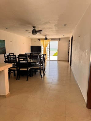 Un vaste espace dédié à la salle à manger, comprenant une table et des chaises, un ventilateur de plafond et une vue sur l’océan grâce à une grande fenêtre.