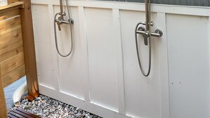 Un box de ducha con dos cabezales de ducha y un cabezal de ducha de mano, instalado en una pared con revestimiento horizontal.
