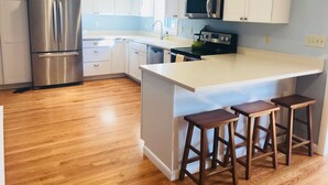 Una cocina moderna con armarios blancos, electrodomésticos de acero inoxidable y taburetes de bar de madera.