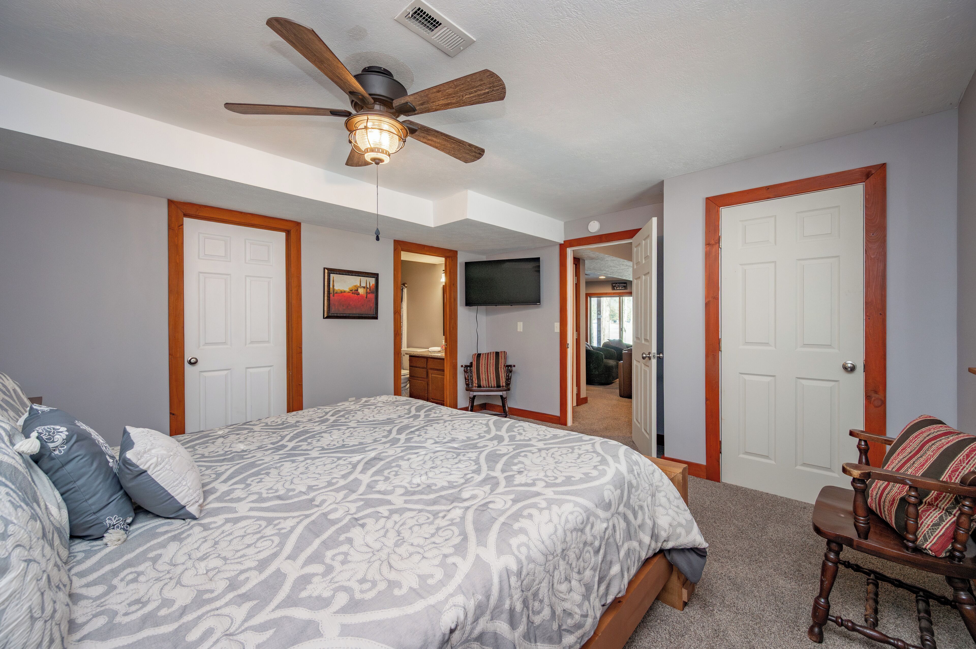A bedroom with a large bed, a ceiling fan, a television, and a door leading to another room.