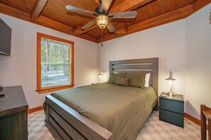 Camera da letto con soffitto in legno, un letto con testiera, un comodino con lampada e una finestra con persiane.