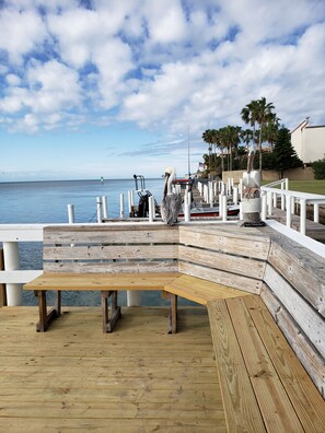 A wooden pier with a bench and a sculpture, overlooking a calm sea with palm trees and a clear sky. - Home Away from Home, Sit Back, Relax, The Beach and Bay are in Your Back Yard (South Padre Island)