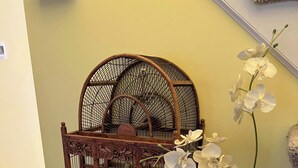 Una jaula de pájaro de madera con intrincados grabados, una orquídea en maceta y un libro abierto con una pluma sobre un mantel a cuadros.