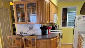 Una cocina con armarios de madera, una isla central con sillas, un refrigerador y una ventana con persianas.