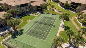 An aerial view of a tennis court surrounded by buildings and palm trees.
