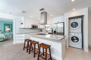 A modern kitchen with white cabinets, a stainless steel refrigerator, a built-in microwave, and a double-washer unit.