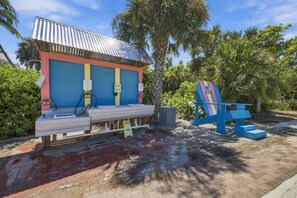 A small, colorful outdoor structure with a metal roof, a bench, and a trash can.