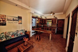 A living room with a sofa, coffee table, and a kitchen area with cabinets and a dining table. - Walk to Beach | 2BR Townhouse w/ Pool and Workspace (Tamarindo)
