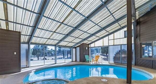 En indendørs swimmingpool med glastag, store vinduer og udsigt til det fri.