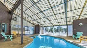 Et overdækket swimmingpool med glasvægge, stole og udsigt til træer.